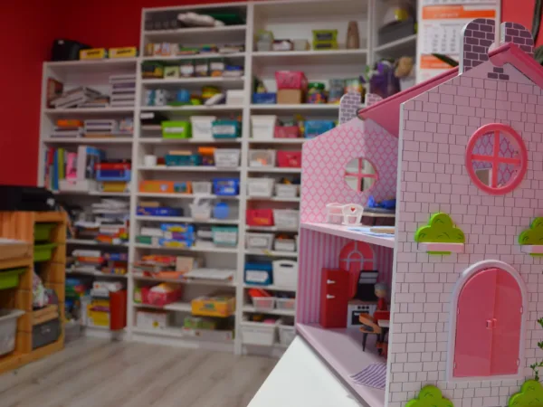 Drewniany domek dla lalek i regały z pomocami do terapii mowy