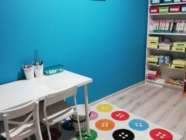 Sala terapeutyczna z turkusową ścianą, białym stolikiem i dywanem w kolorowe guziki