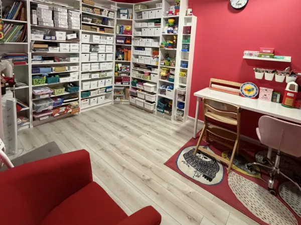 Sala terapeutyczna z czerwoną ścianą, regałami z posegregowanymi pomocami i biurkiem